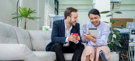 Two individuals seated on a couch, engaged in viewing content on a tablet device together.