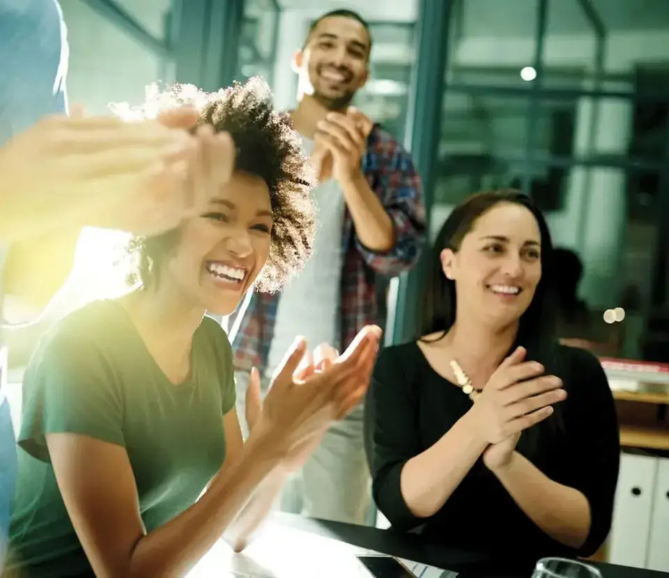 A diverse group of individuals enthusiastically applauding during a meeting, showcasing engagement and support for the speaker.