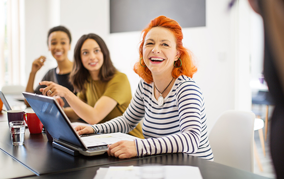 A group of women engaged in discussion while working on laptops at a table, showcasing collaboration and productivity.