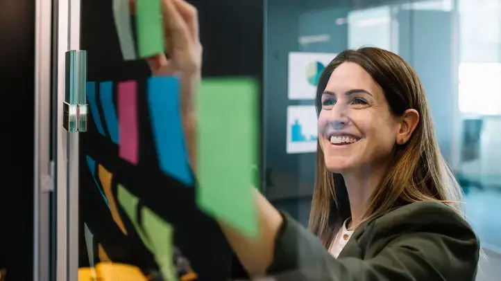 A woman smiles joyfully as she gazes at a glass wall, reflecting her positive demeanor and bright surroundings.