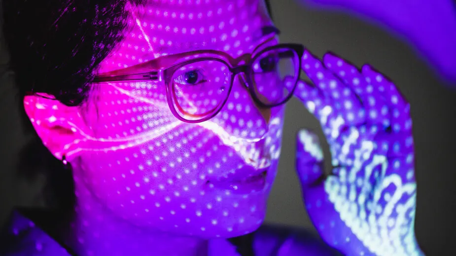 A woman with glasses illuminated by a soft purple light, creating a serene and contemplative atmosphere.