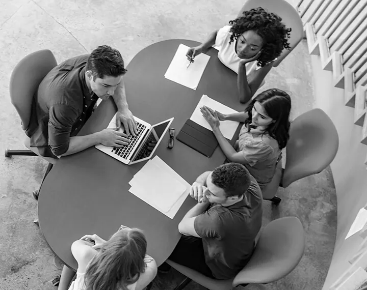 A diverse group of individuals collaborating around a table, each using their laptops for a productive discussion.
