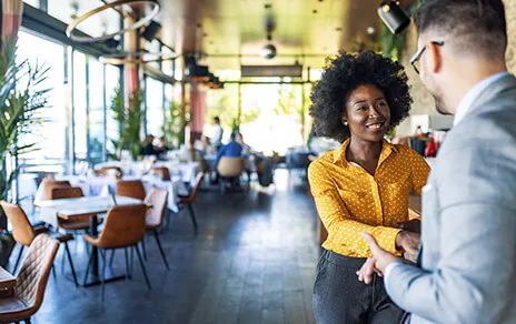 A man and woman stand together in a restaurant, engaged in conversation amidst a warm and inviting atmosphere.
